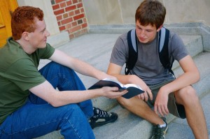 Two Young Men Sitting On Public School Steps Discussing The Bible